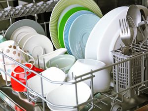 Open dishwasher with loaded plates, bowls, cups, and cutlery