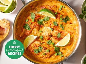 A pan of a cooked dish garnished with lime wedges herbs and sauce