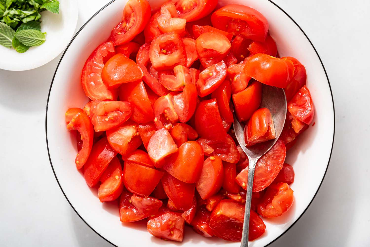 tomato quarter in a large bowl next to a smaller bowl with minced herbs for 5-ingredient tomato salad recipe