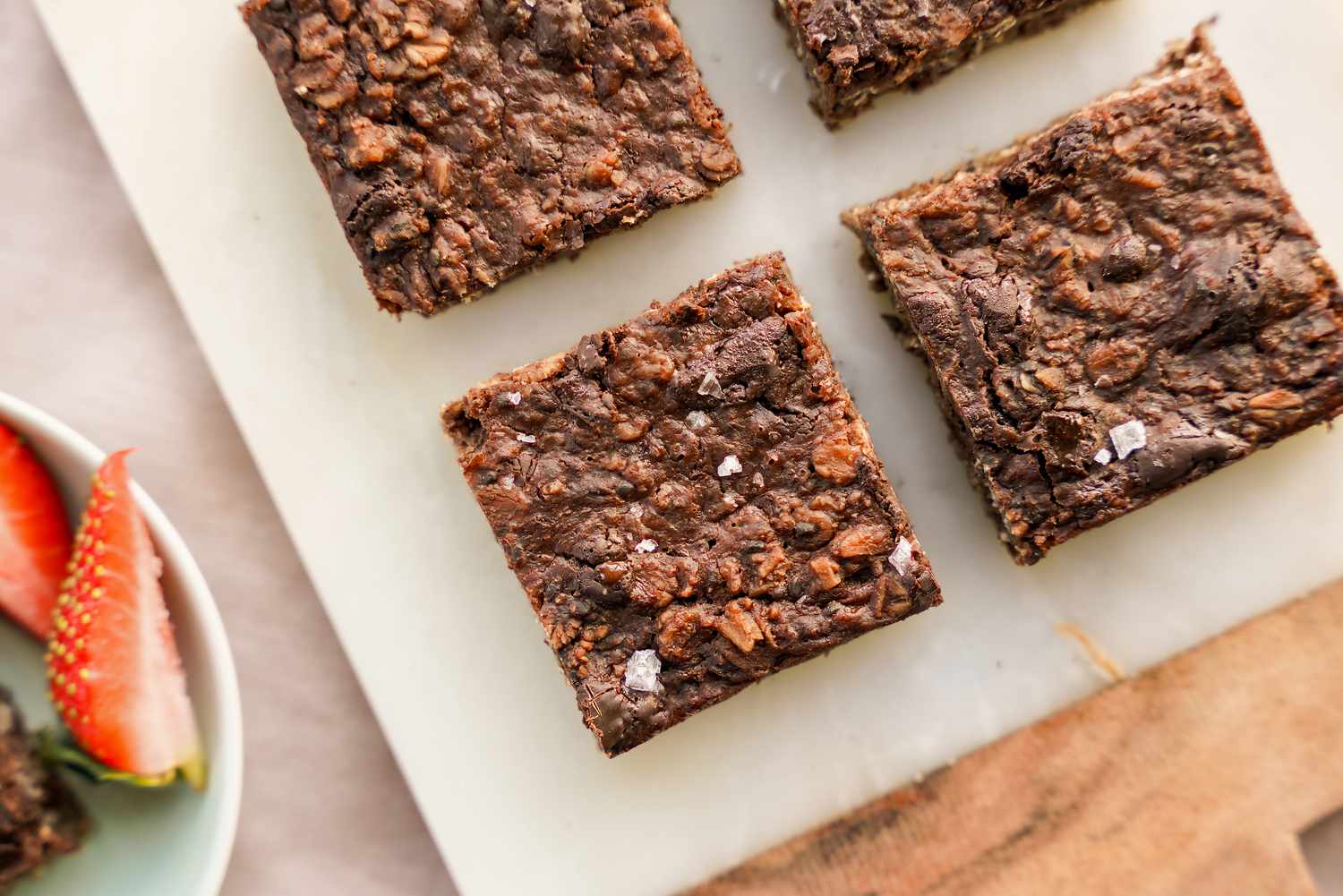 Vegan Brownie Baked Oatmeal on a Marble Counter Next to a Bowl with a Brownie and Quartered Strawberries