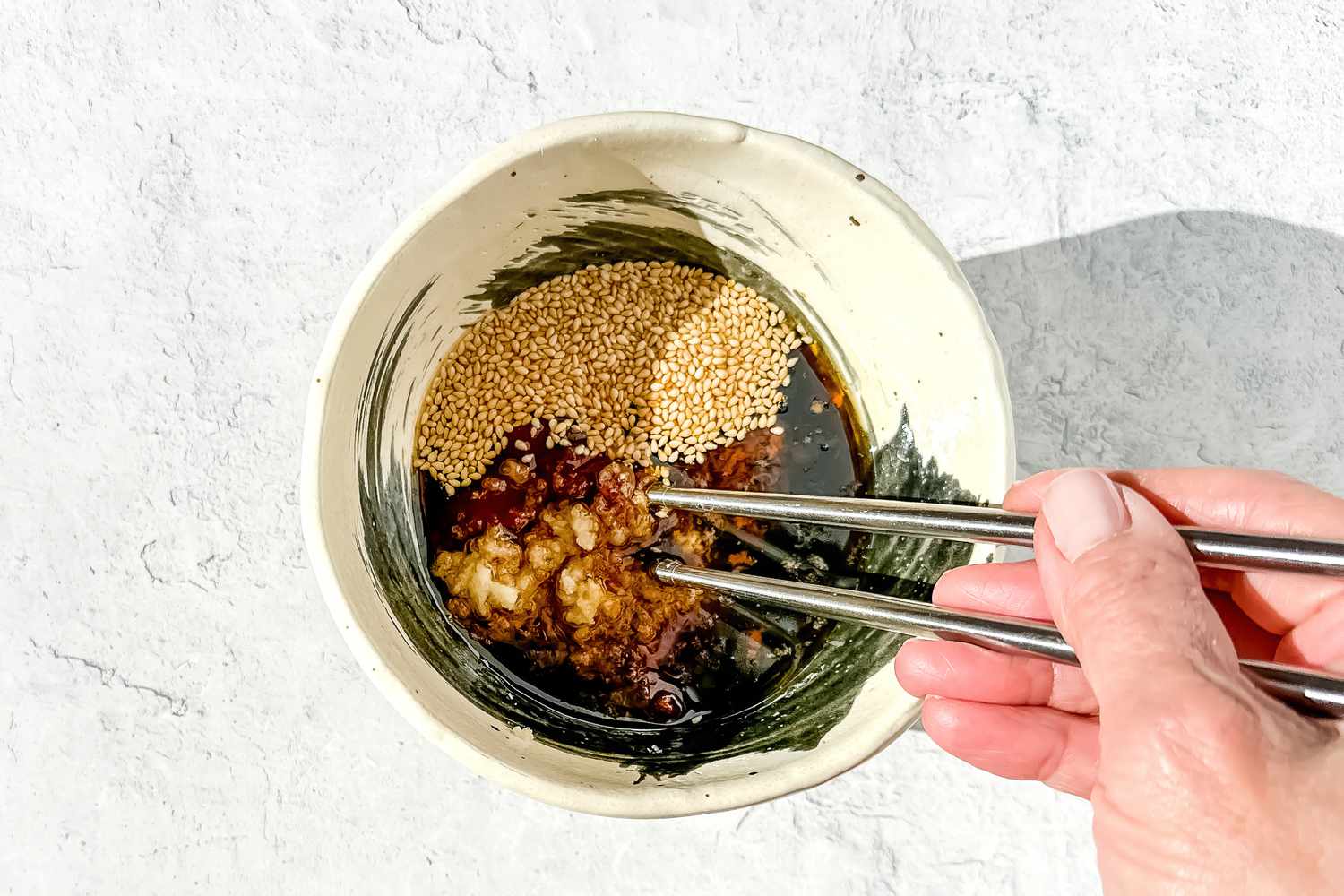 Bowl of Spicy Gochujang Sauce Ingredients (Garlic, Toasted Sesame Seeds, Soy Sauce, Gochujang, etc). Mixed Together Using a Pair of Chopsticks Naengmyeon