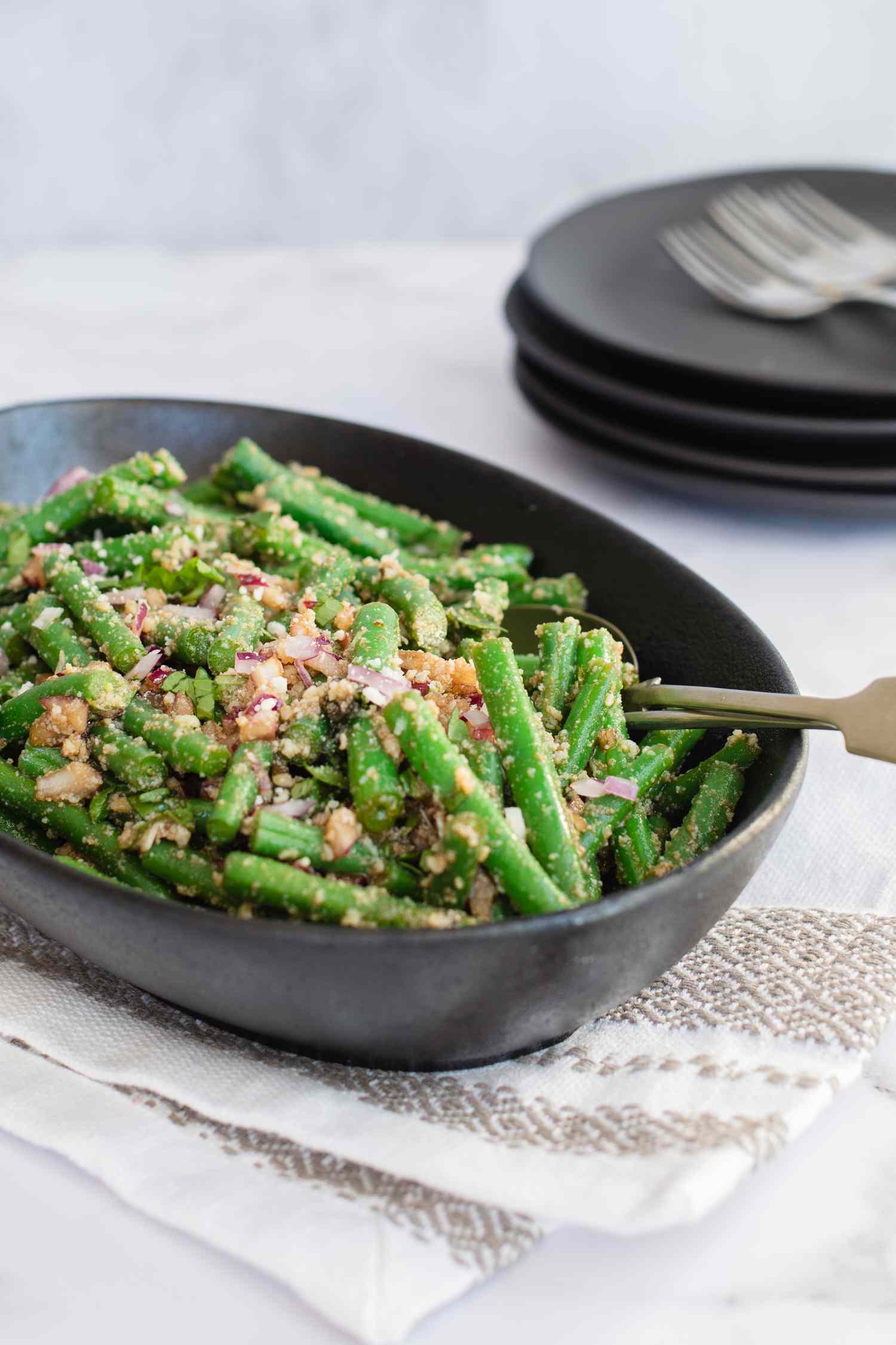 Side view of green bean salad in a serving bowl with plates behind it.