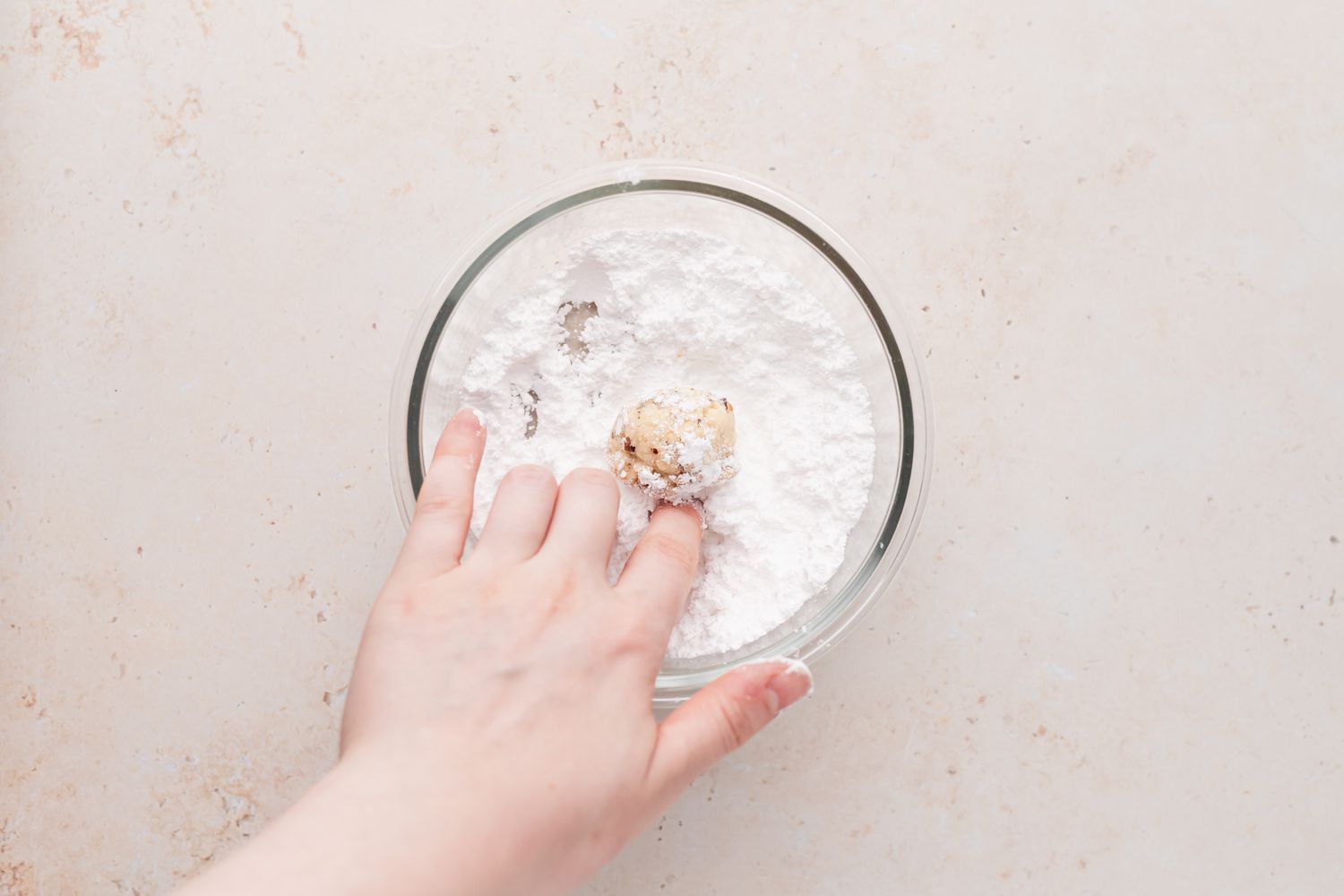 Rolling snowball cookies in powdered sugar for a walnut cookies recipe.