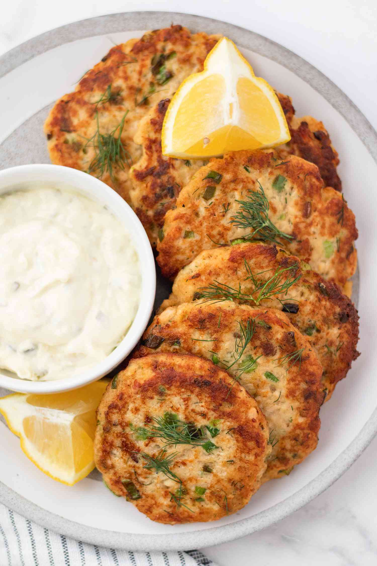 Salmon patties set on a plate with a dip and lemon.