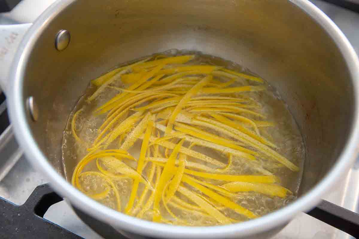Lemon zest strips in boiling water for candied peel