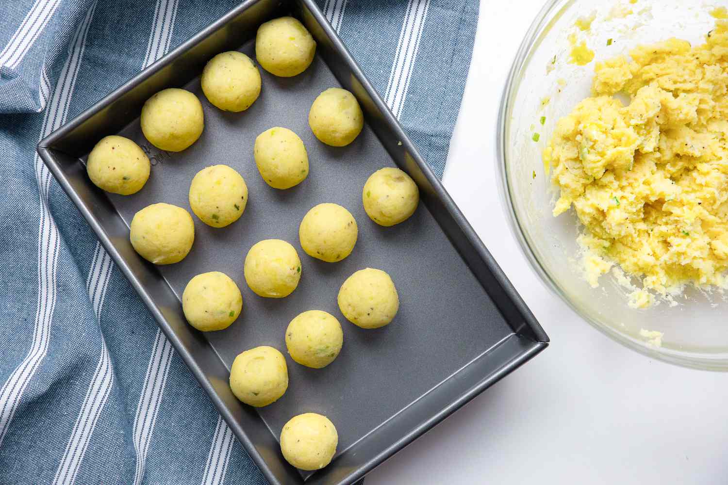 Potato Croquette Filling Rolled into Balls and Placed in a Baking Pan Next to a Bowl of Croquette Filling