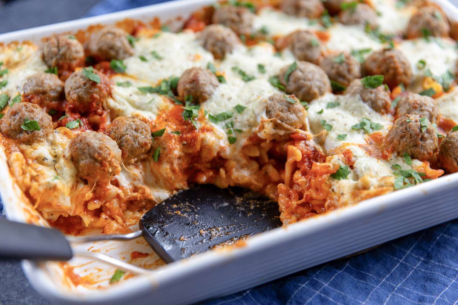 A baked pasta dish topped with meatballs and cheese partially served