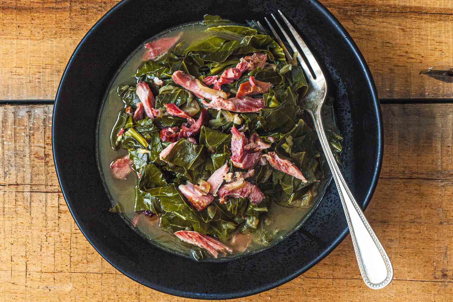 Overhead view of southern collard greens in a black bowl on a wood surface.