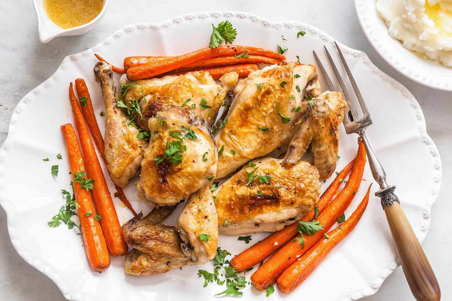 Overhead view of a white platter of roasted chicken breasts, legs, thighs and wings, cooked carrots and a serving fork on a marble countertop