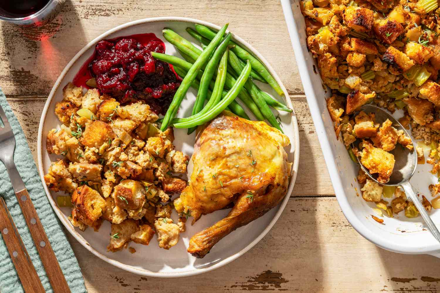 Thanksgiving dinner plate with roasted turkey stuffing green beans and cranberry sauce alongside a dish of extra stuffing