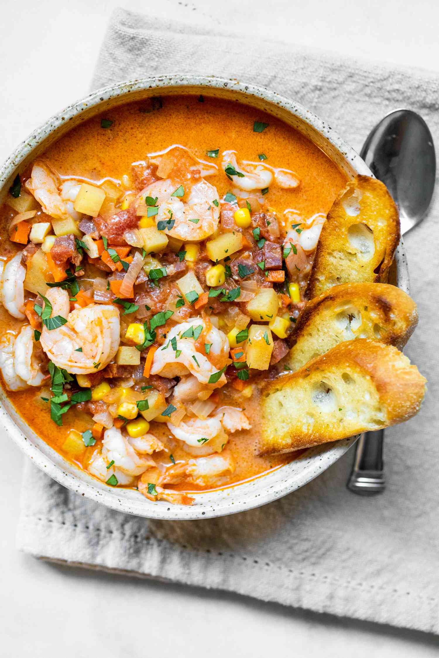 Bowl of Shrimp and Chorizo Chowder Topped with Parsley and Slices of Toasted Baguette, on a Dinner Napkin