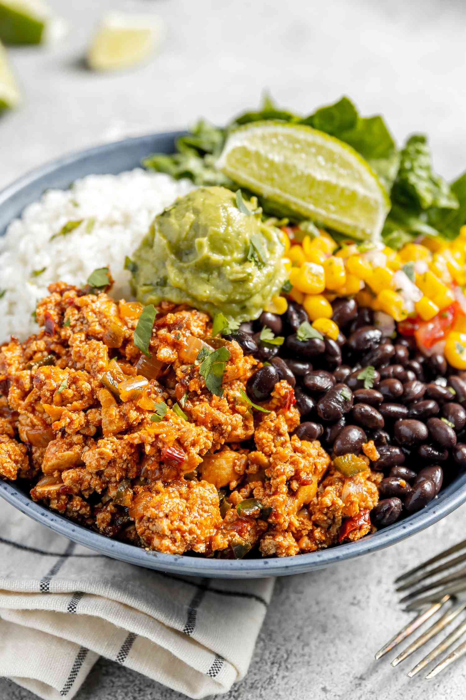 Bowl of Copycat Sofritas Served with Rice, Black Beans, Guacamole, Lettuce, Salsa, and a Lime Wedge