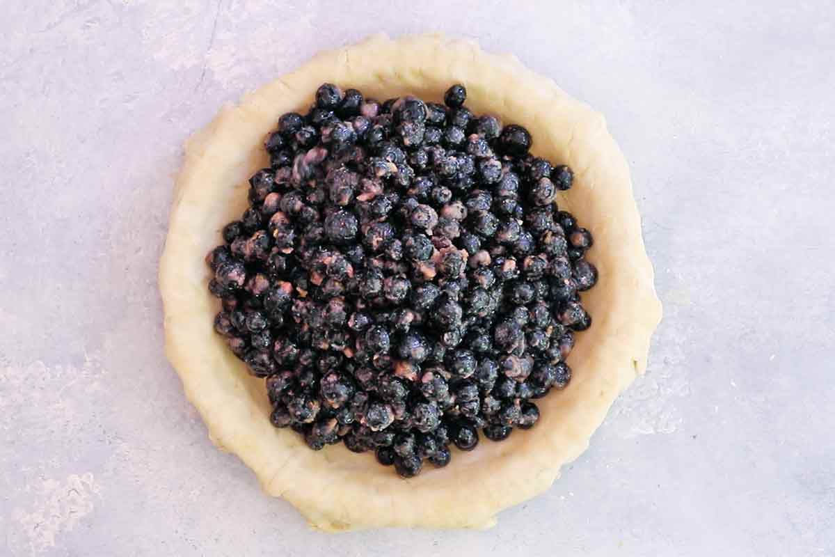 Overhead of coated blueberries resting in an uncooked pie crust