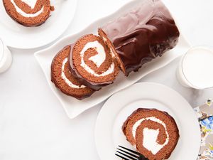 Overhead view of a chocolate cake roll and a plate with a slice on it.