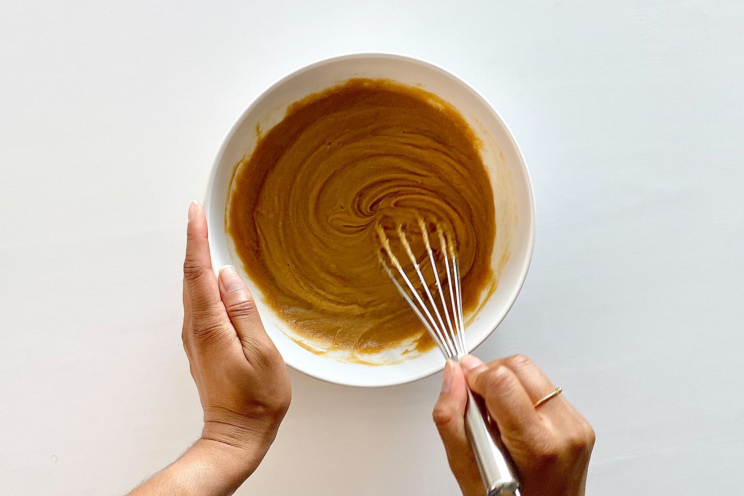 Whisking sugars and egg in a bowl to make Gluten-Free Sheet Pan Monster Cookies.