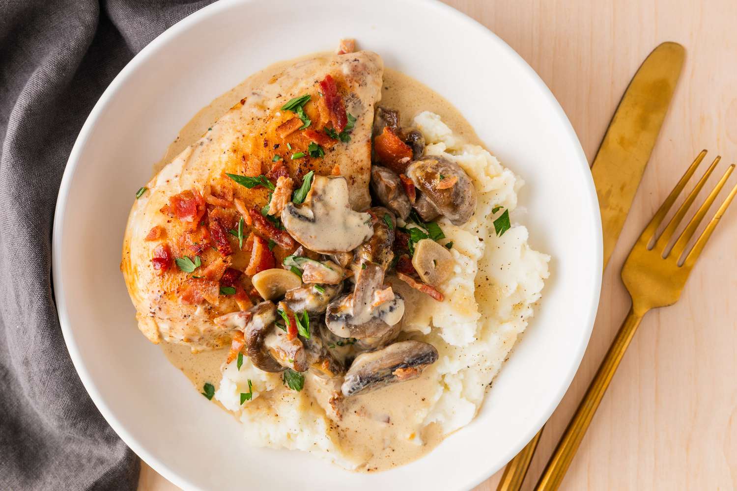 One serving of Chicken Supreme on a plate with knife and fork and napkin on the side