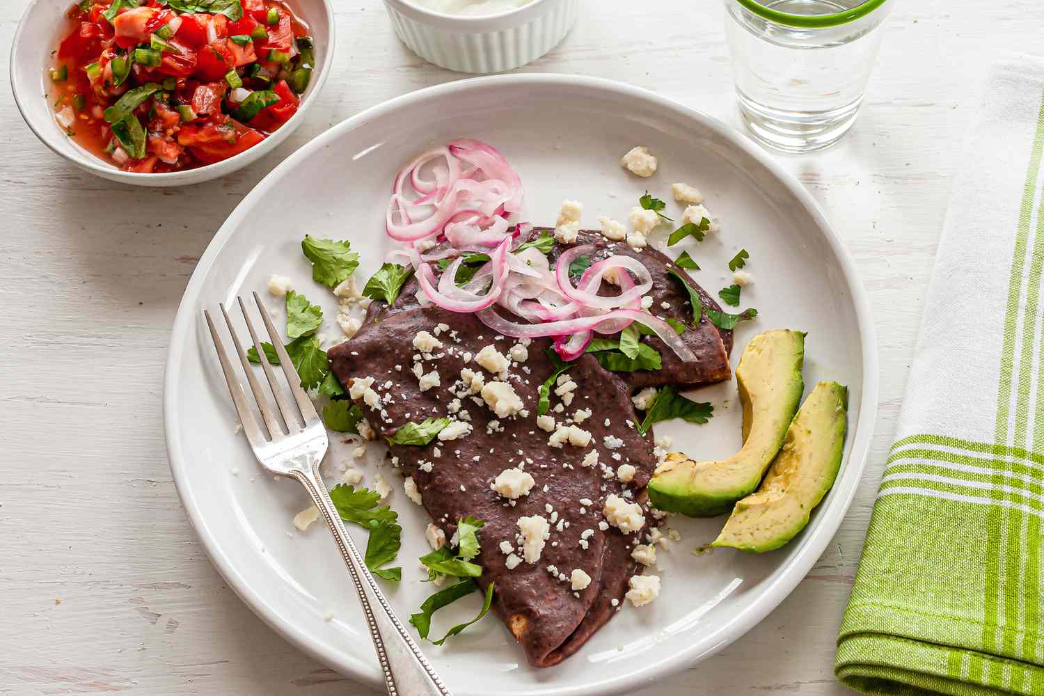 Mexican Enfrijoladas topped with avocado and cotija.
