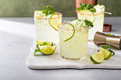 Three margarita glasses with lime garnish and mint leaves on a white tray with lime wedges nearby