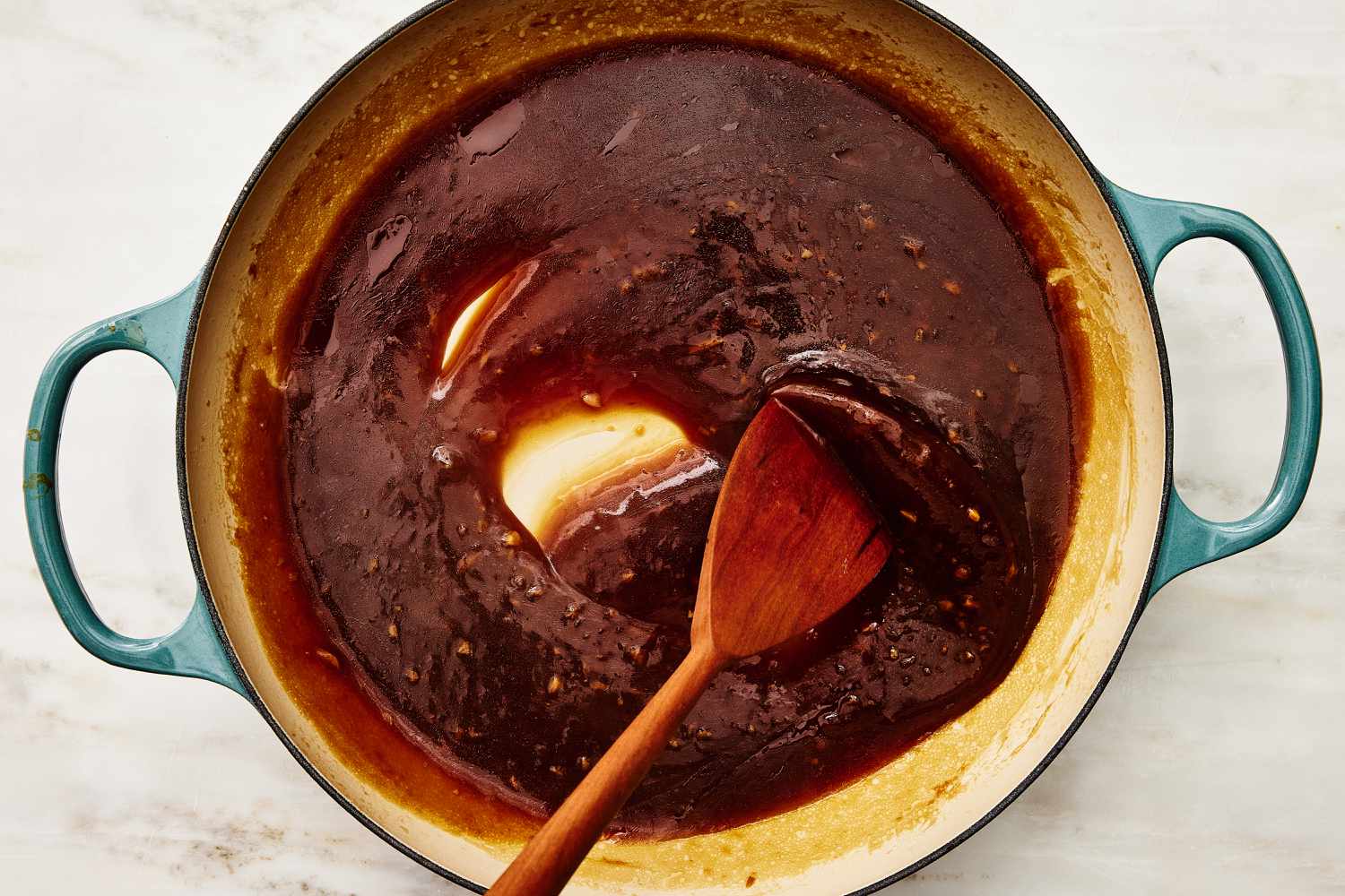 Overhead view of a large pot of soy sauce mixture being stirred with a wooden spoon