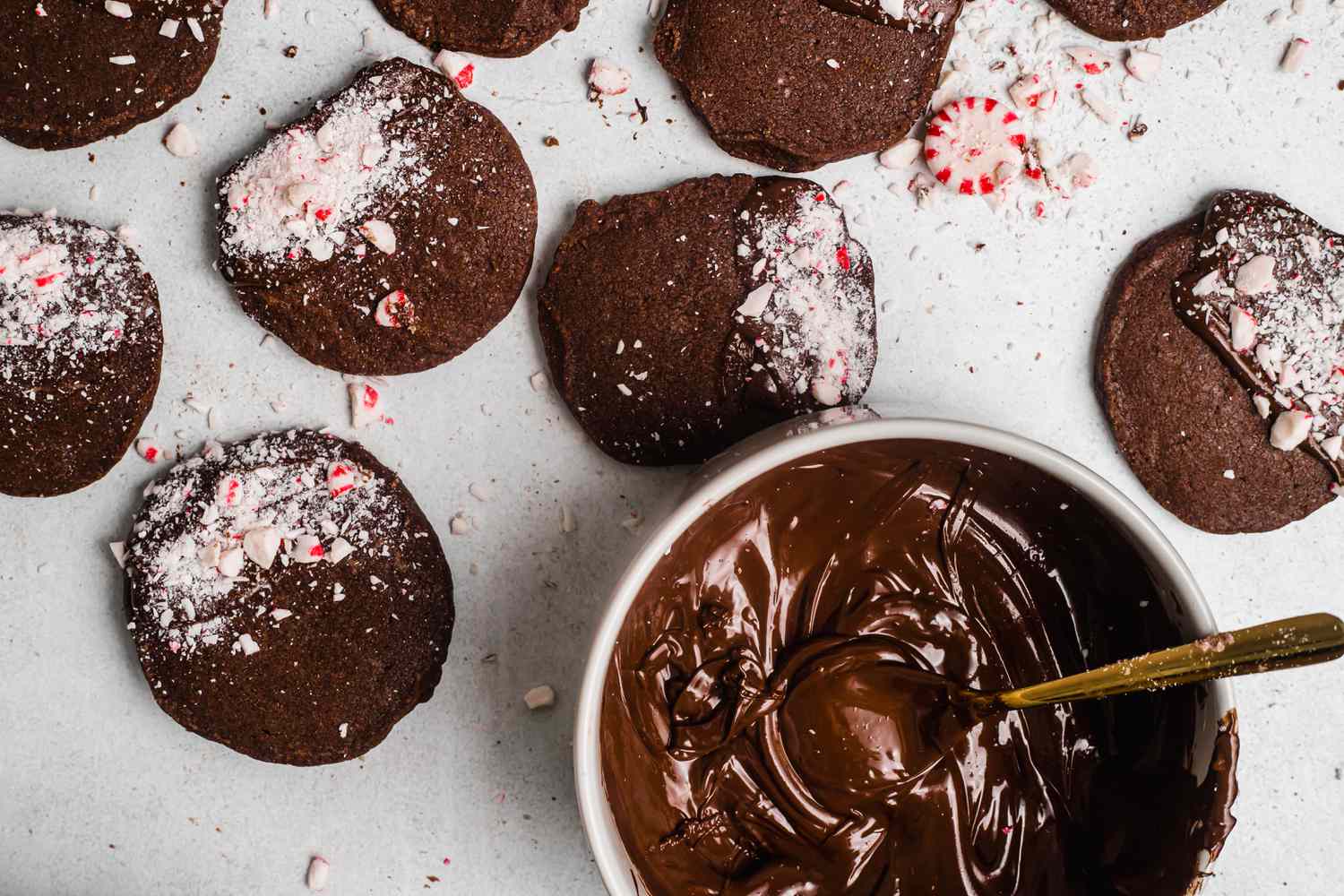 Overhead view of shortbread dipped in chocolate and peppermint on a baking sheet with melted chocolate next to it.