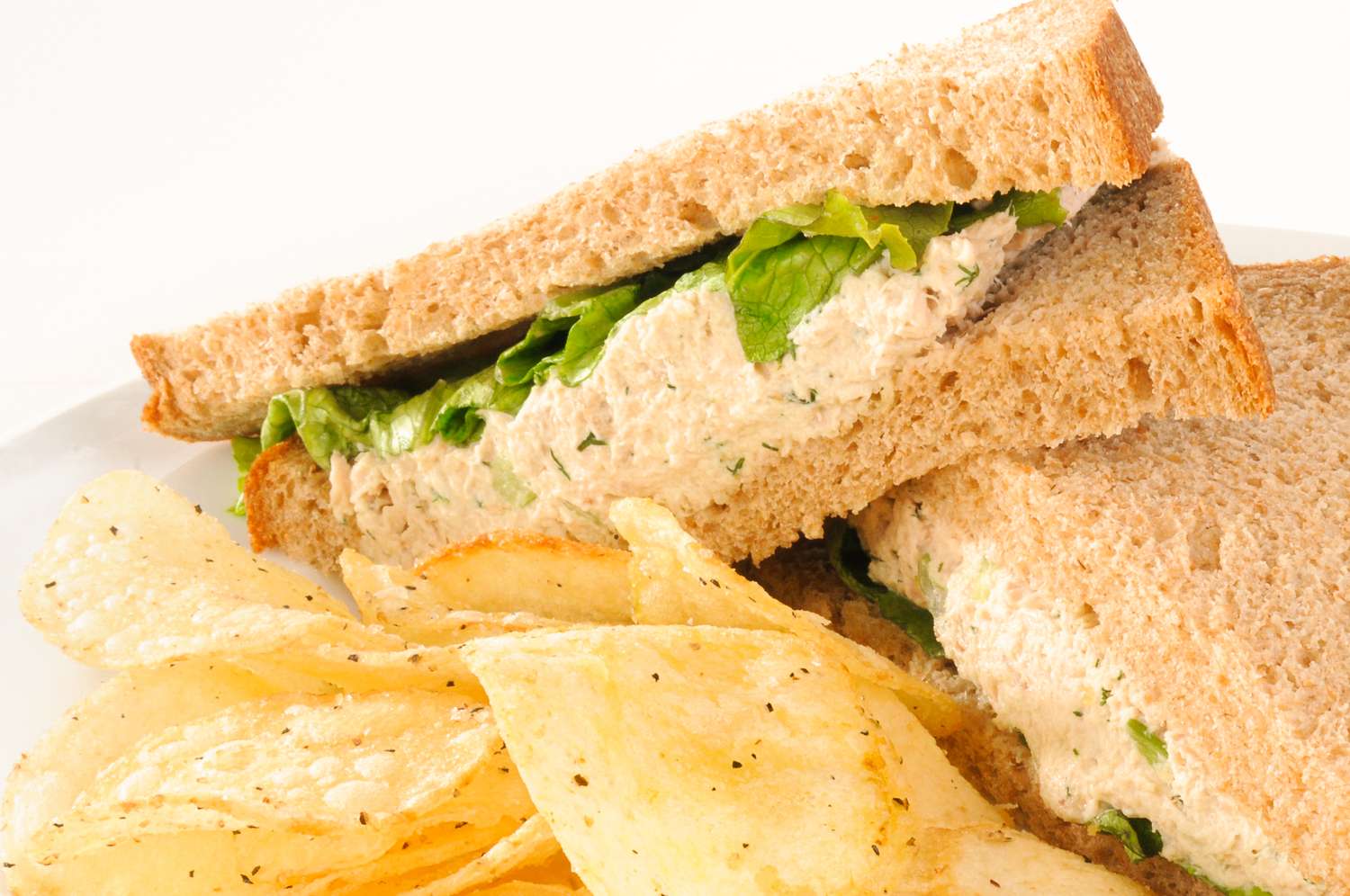 Tuna sandwich with lettuce served alongside potato chips