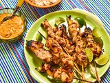Grilled chicken satay skewers with lime wedges, bowl of peanut sauce and rice served on a plate