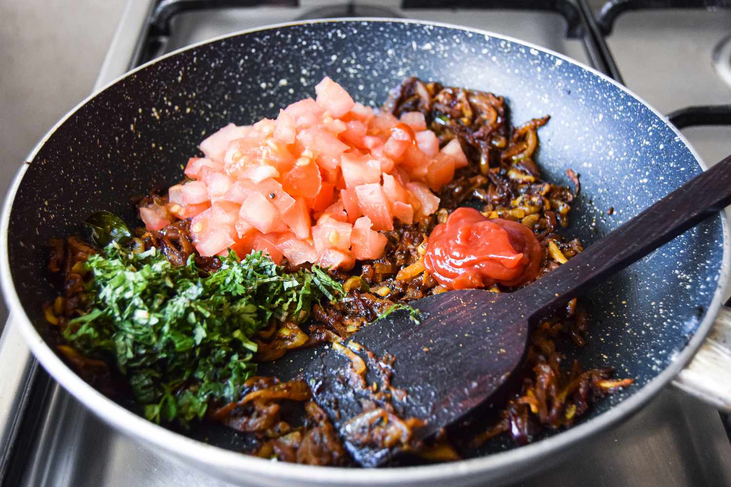 Tomatoes, Ketchup, and Mint Mixed into the Caramelized Onion Mixture Using a Wooden Spatula for Masala Curry Recipe