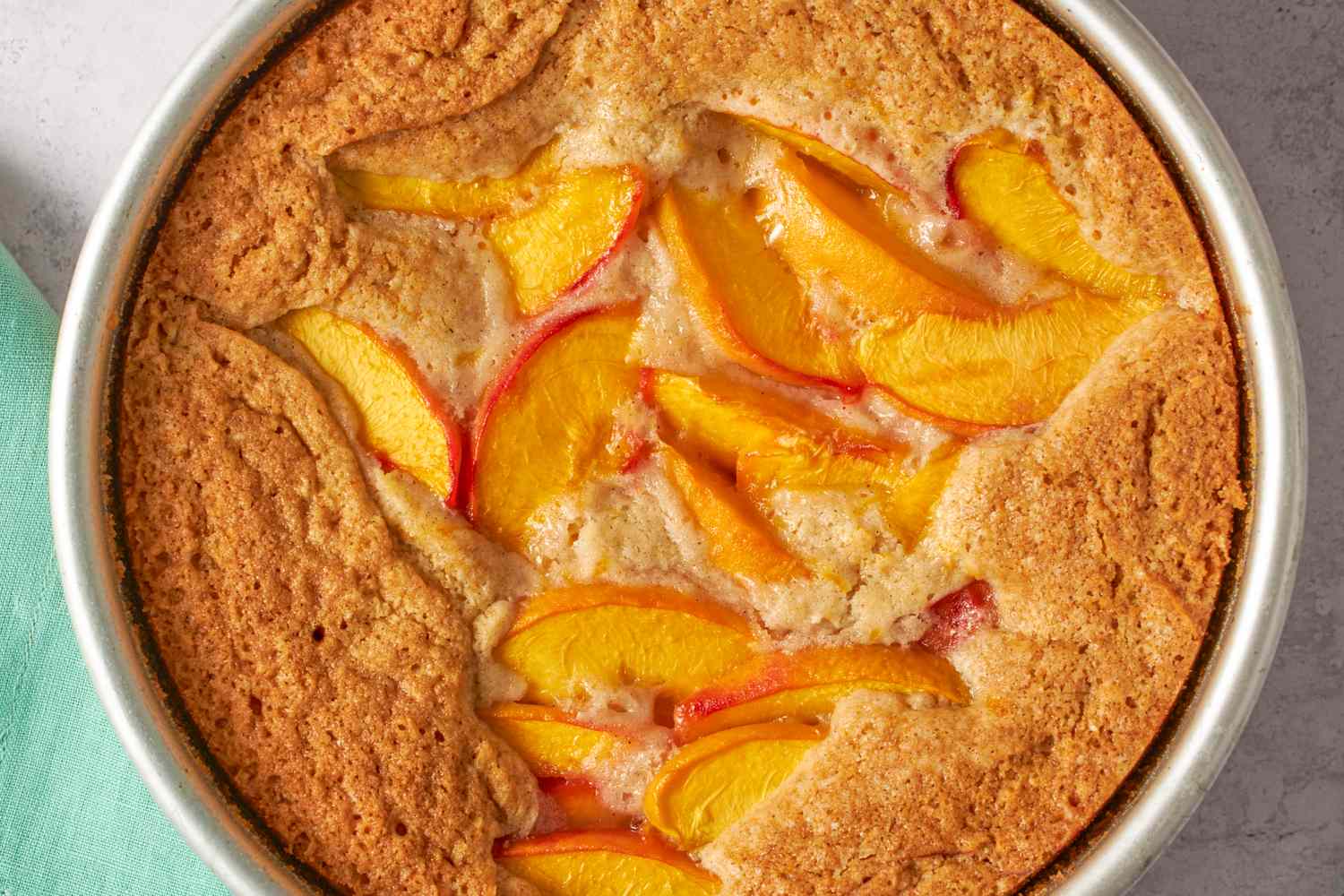 Baked peach spoon cake in a round pan featuring peach slices in a golden uneven cake top