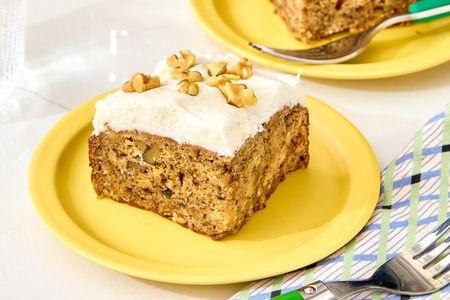 A slice of banana bread cake with frosting and walnuts on a yellow plate
