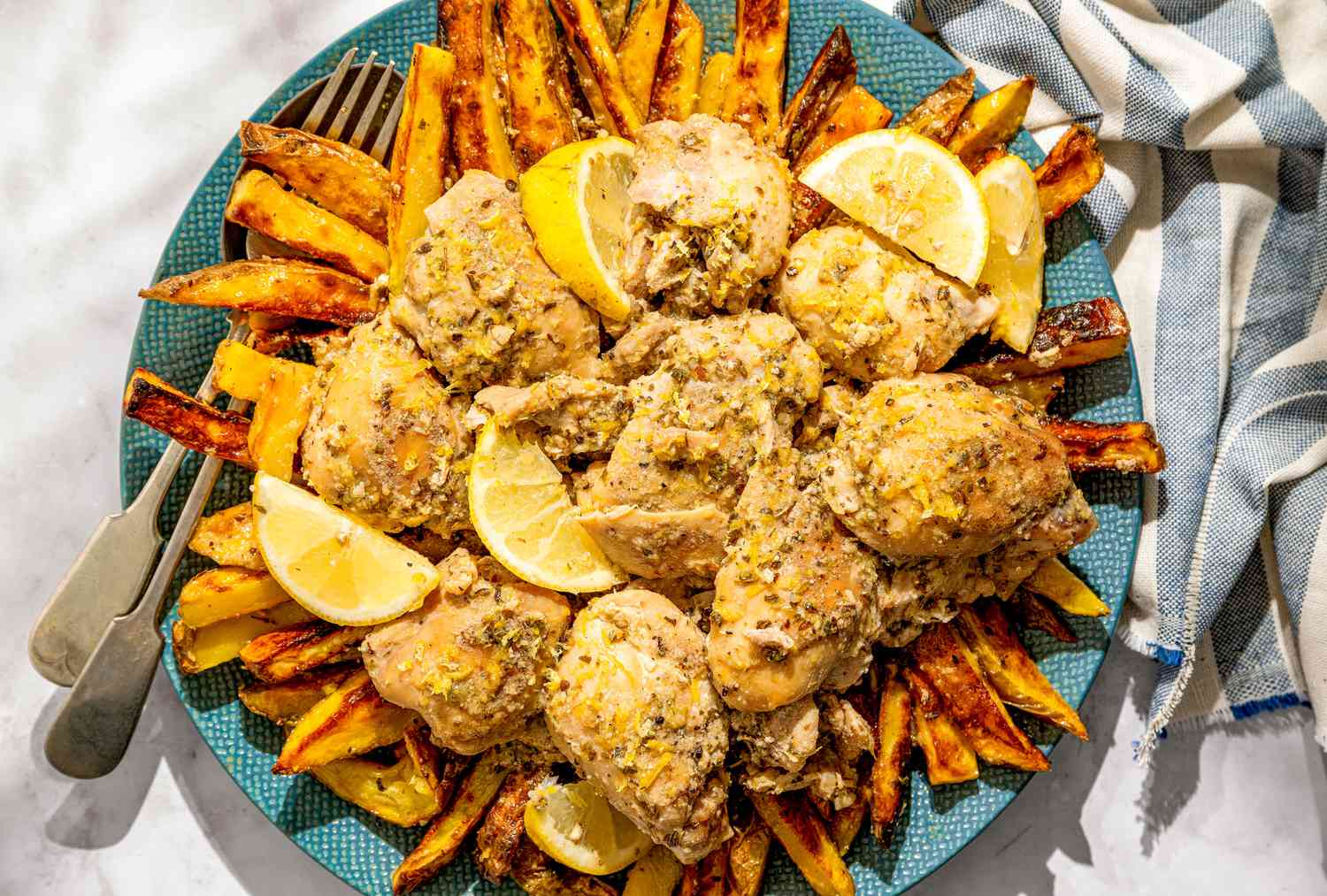 Plate of braised chicken thighs served with fries and lemon slices