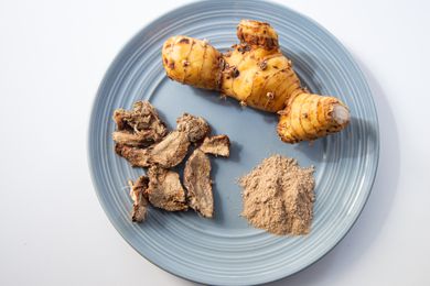 Fresh, dried, and powdered galangal spice on a blue plate