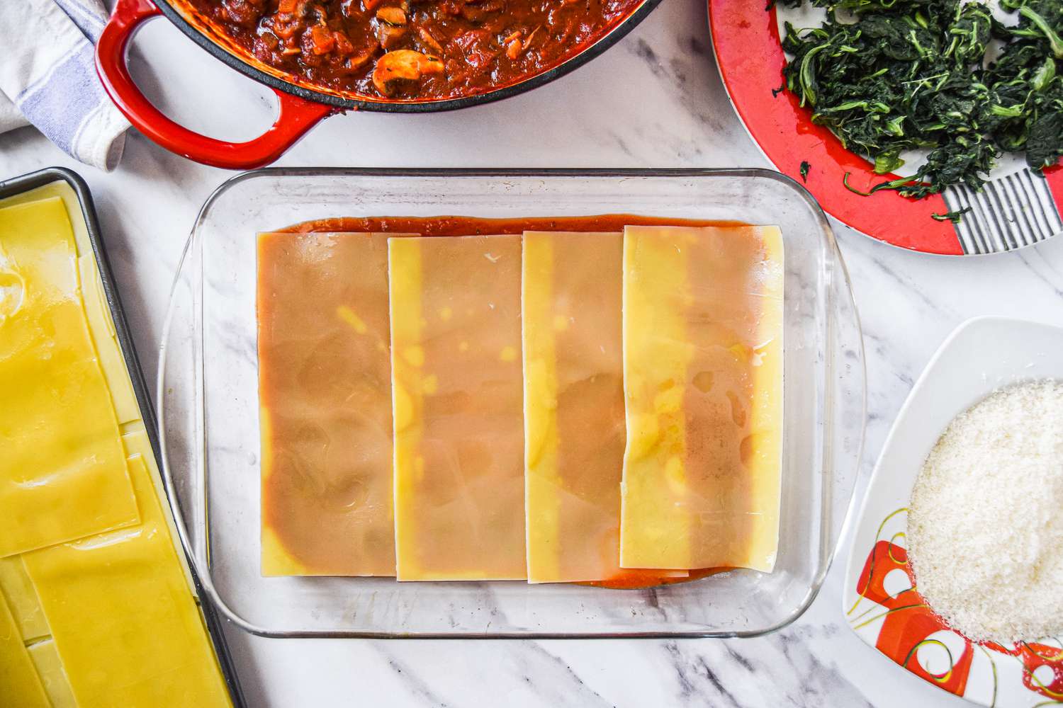 A Layer of Noodles Added to Casserole Dish on top of a red sauce 