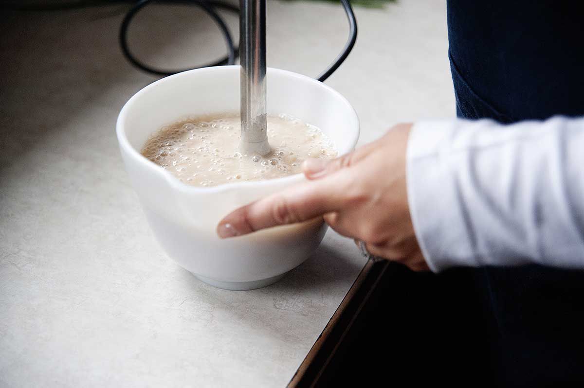 Pureeing beans in a white bowl with an immersion blender for homemade creamy chicken noodle soup