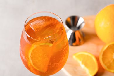 A glass of Aperol spritz garnished with orange slices, with an orange and a jigger in the background