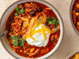 A bowl of chicken enchilada chili topped with sour cream shredded cheese beans and cilantro