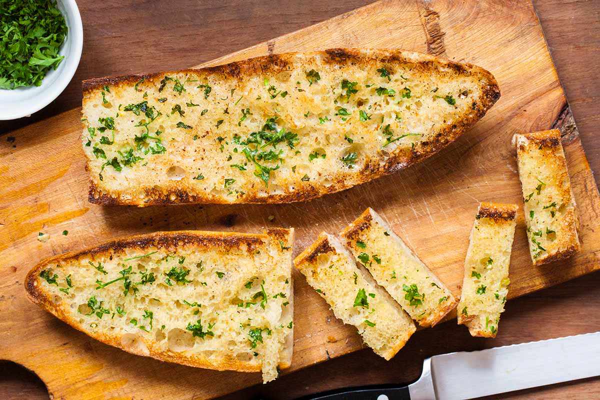 A loaf of garlic bread on a cutting board, partially cut into slices