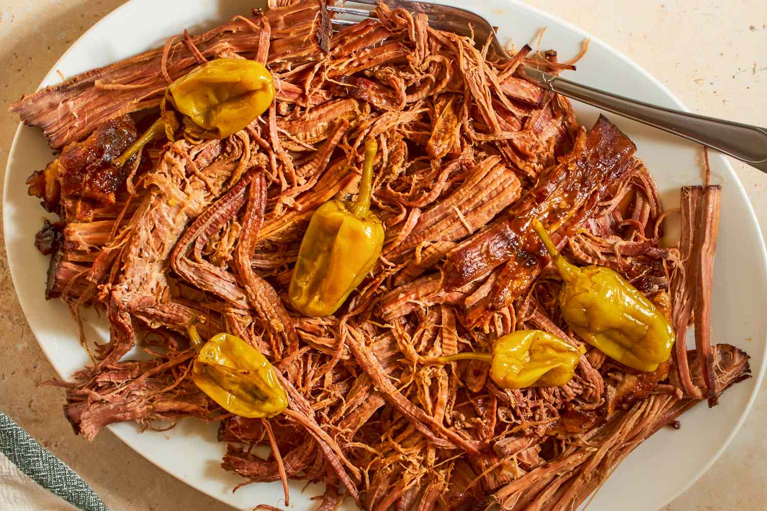 Shredded pot roast on a plate with pepperoncini peppers fork to the side