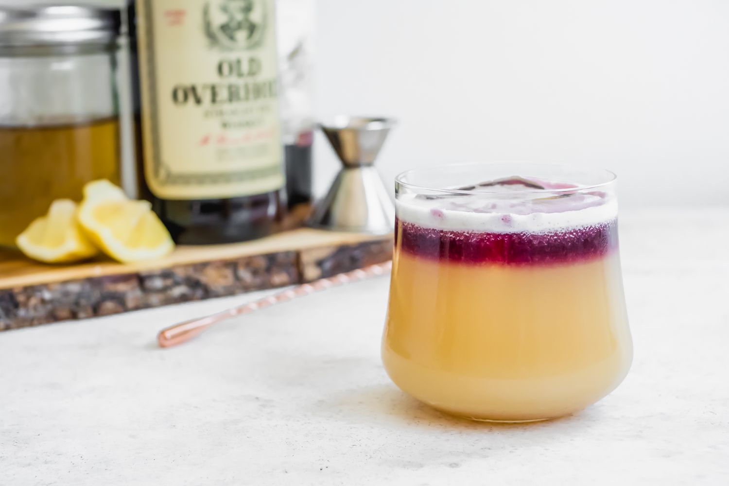 New York Sour Cocktail with Ingredients (Bottle of Whiskey, Lemon Wedges, Jar of Simply Syrup, etc) and Bartender Supplies in the Background