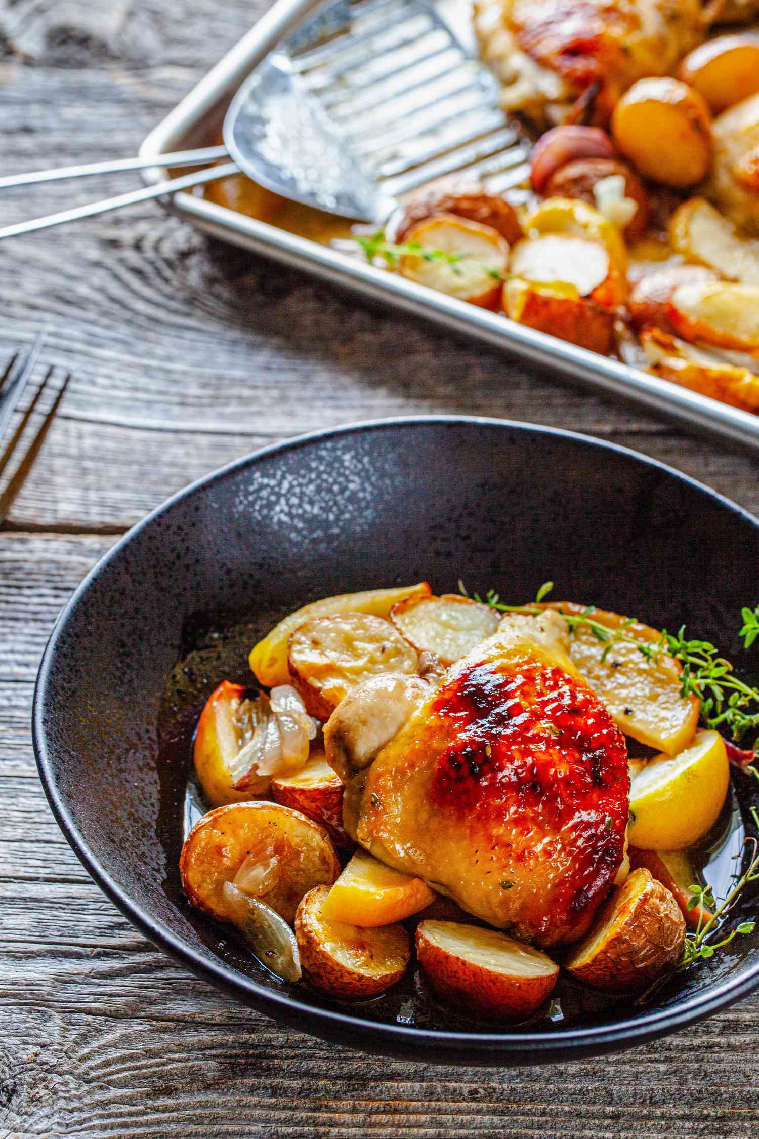 Bowl of Sheet Pan Honey Roasted Chicken Thighs with Baby Potatoes, Apples, Shallots, and Thyme with the Rest in the Background