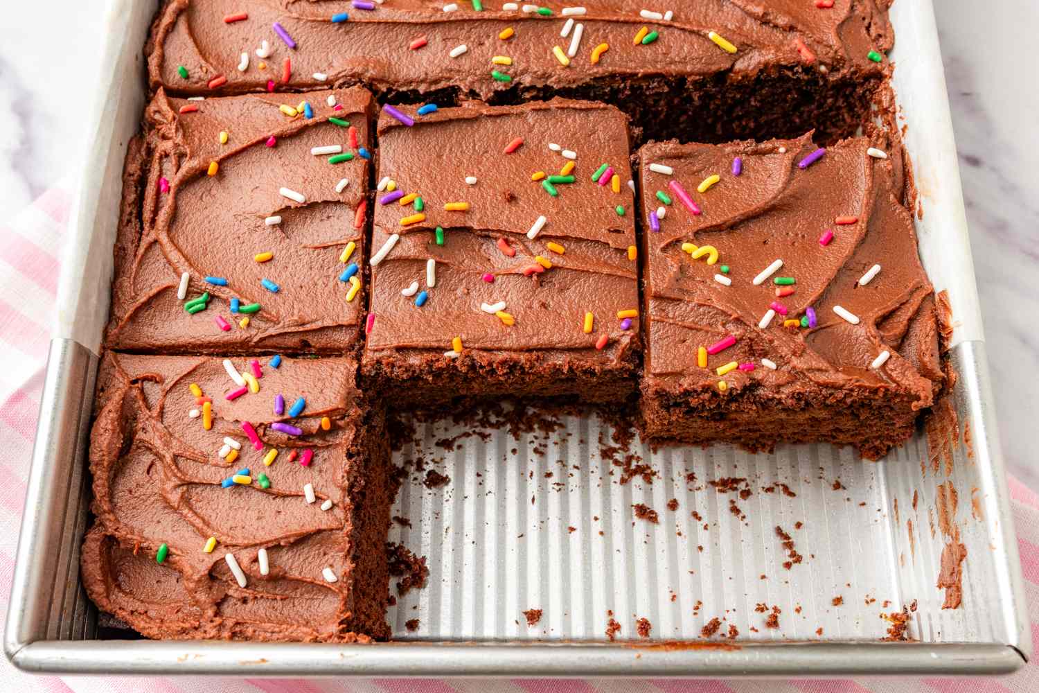 A chocolate cake in a rectangular baking pan with chocolate frosting and colorful sprinkles partially cut into squares