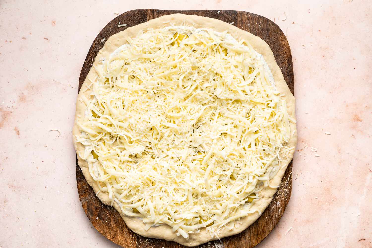 cheese on top of a pickle pizza in progress