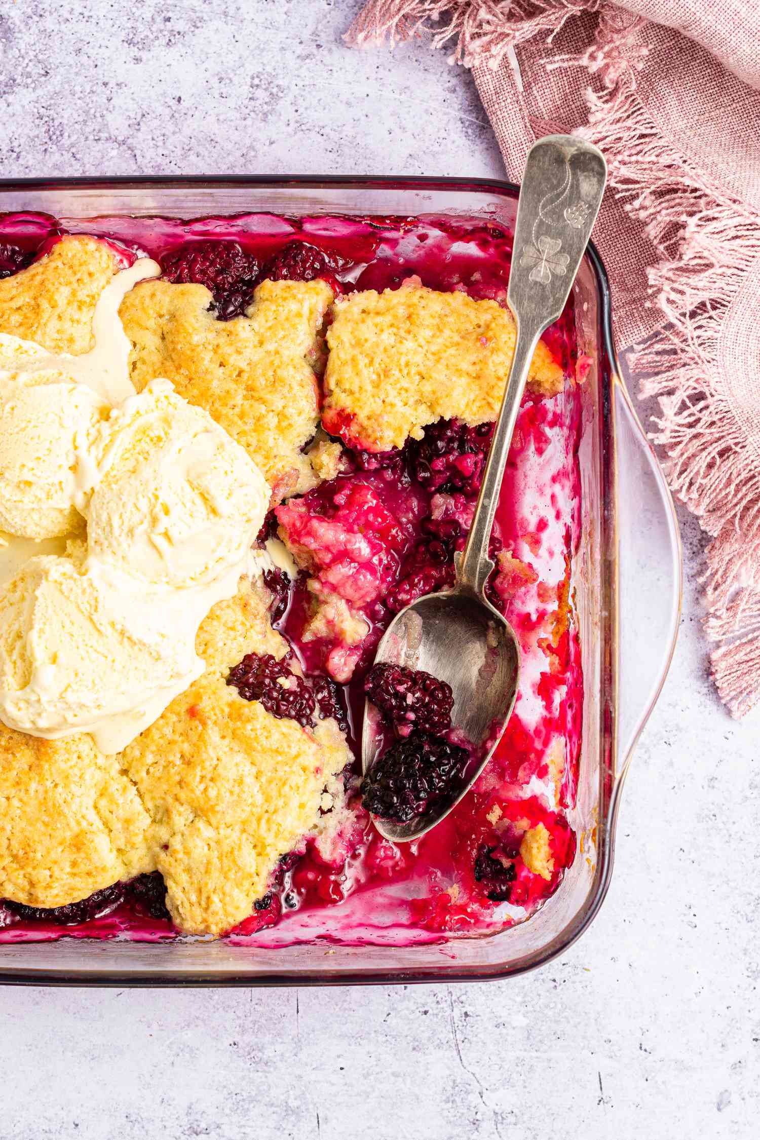 Overhead view of a baking dish with a serving removed from the blackberry cobbler and with a couple scoops of vanilla ice cream on top.