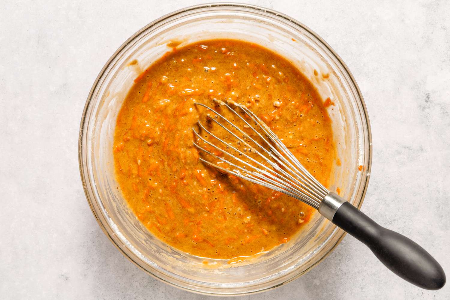 Carrot cake batter in a glass bowl with a whisk resting inside, ready for baking preparation.