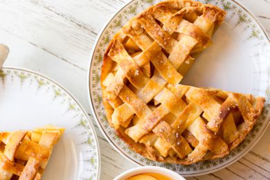 Overhead view of a plate with an apple pie with a slice removed next to another plate with a slice all on a white wooden tabletop