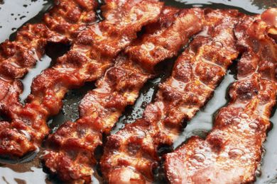 Deeply browned and crisp-looking slices of bacon cooking in a cast iron skillet