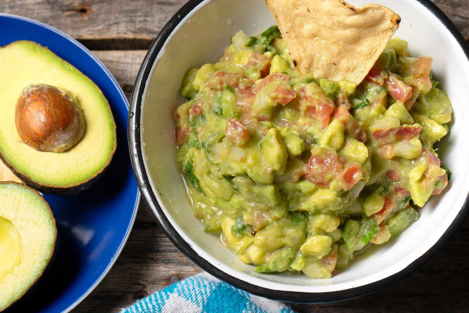 A bowl of guacamole with a tortilla chip dipped, and avocado halves on the side