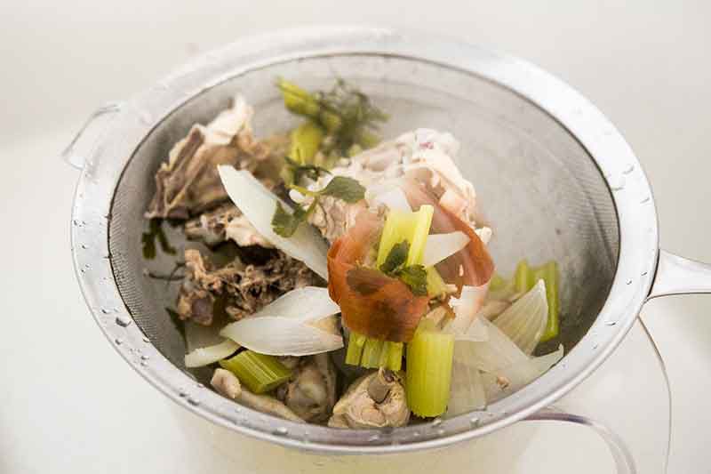 Straining vegetables out of broth for homemade chicken noodle soup.