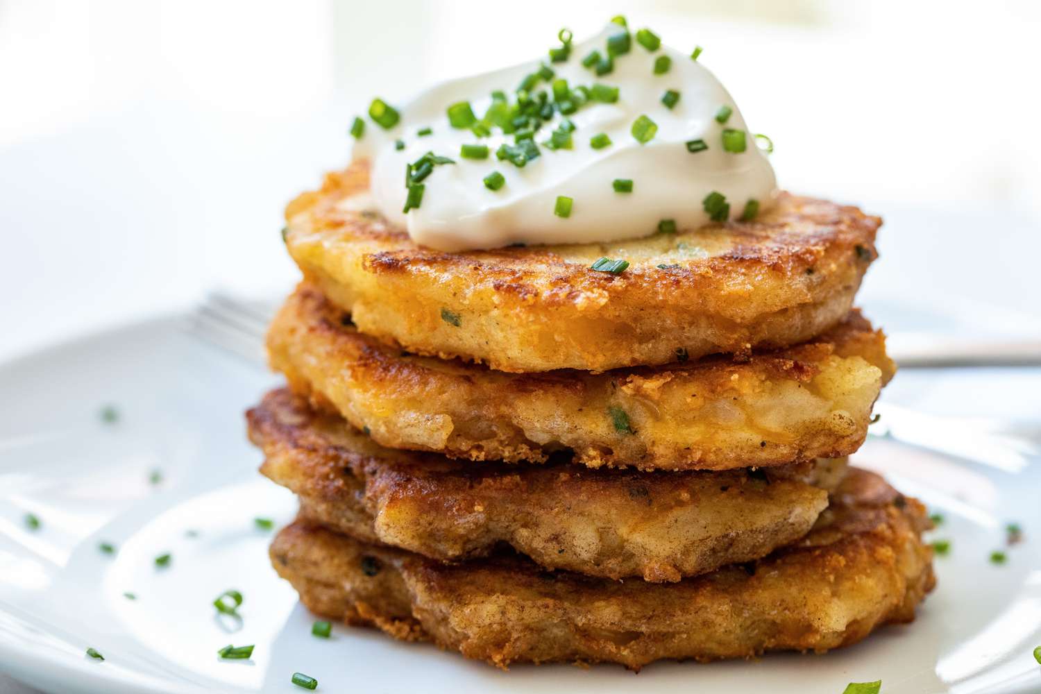 Leftover mashed potato pancakes stacked on a plate and topped with sour cream and chives.