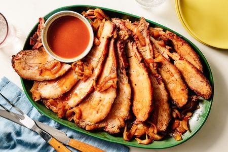 A platter of sliced brisket with onions and a dipping sauce in a small bowl