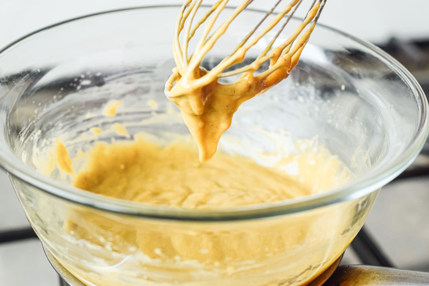 Whisk held above a bowl of custard for a sabayon recipe.